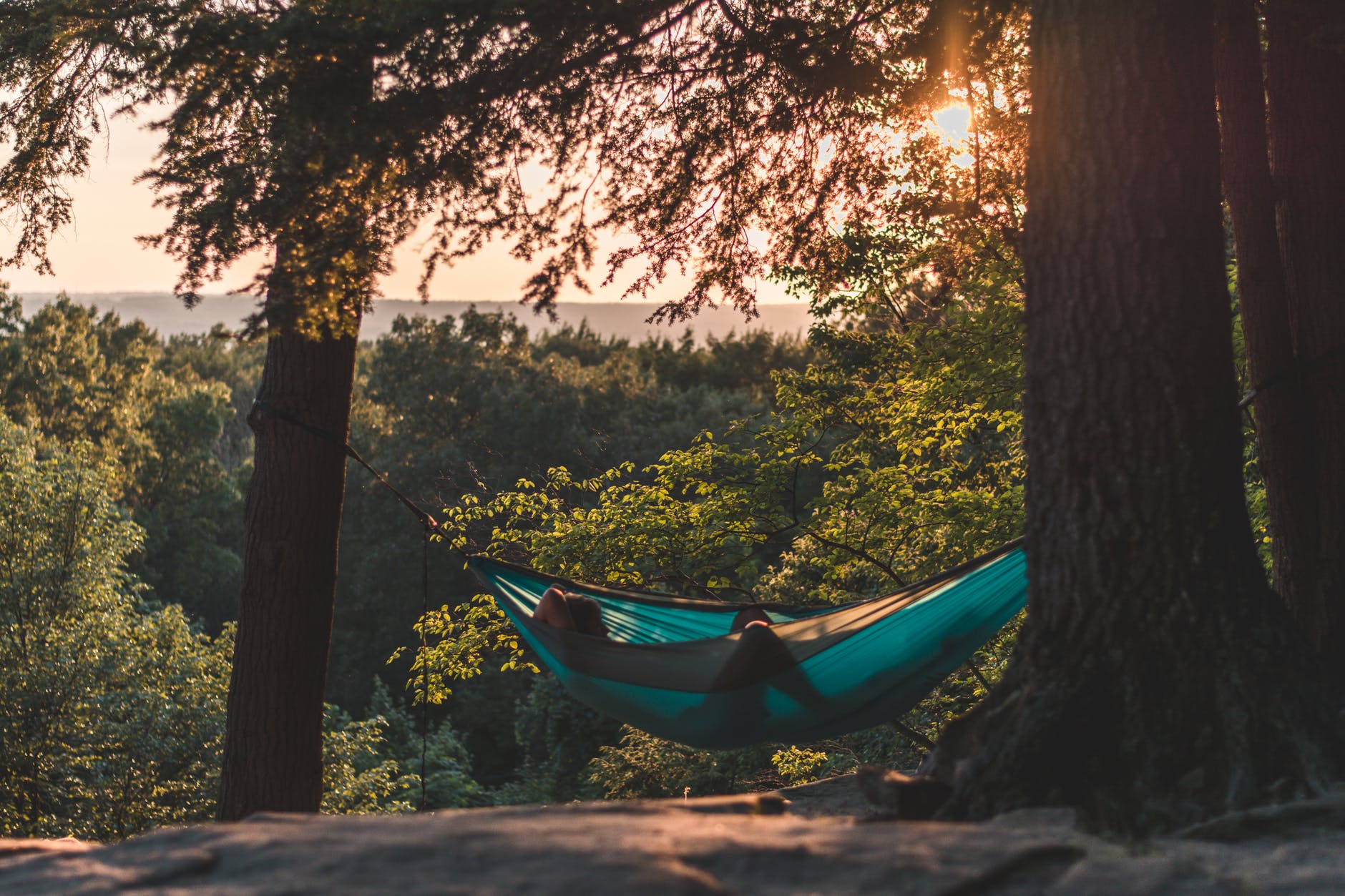 person lying on hammock between trees at daytime
